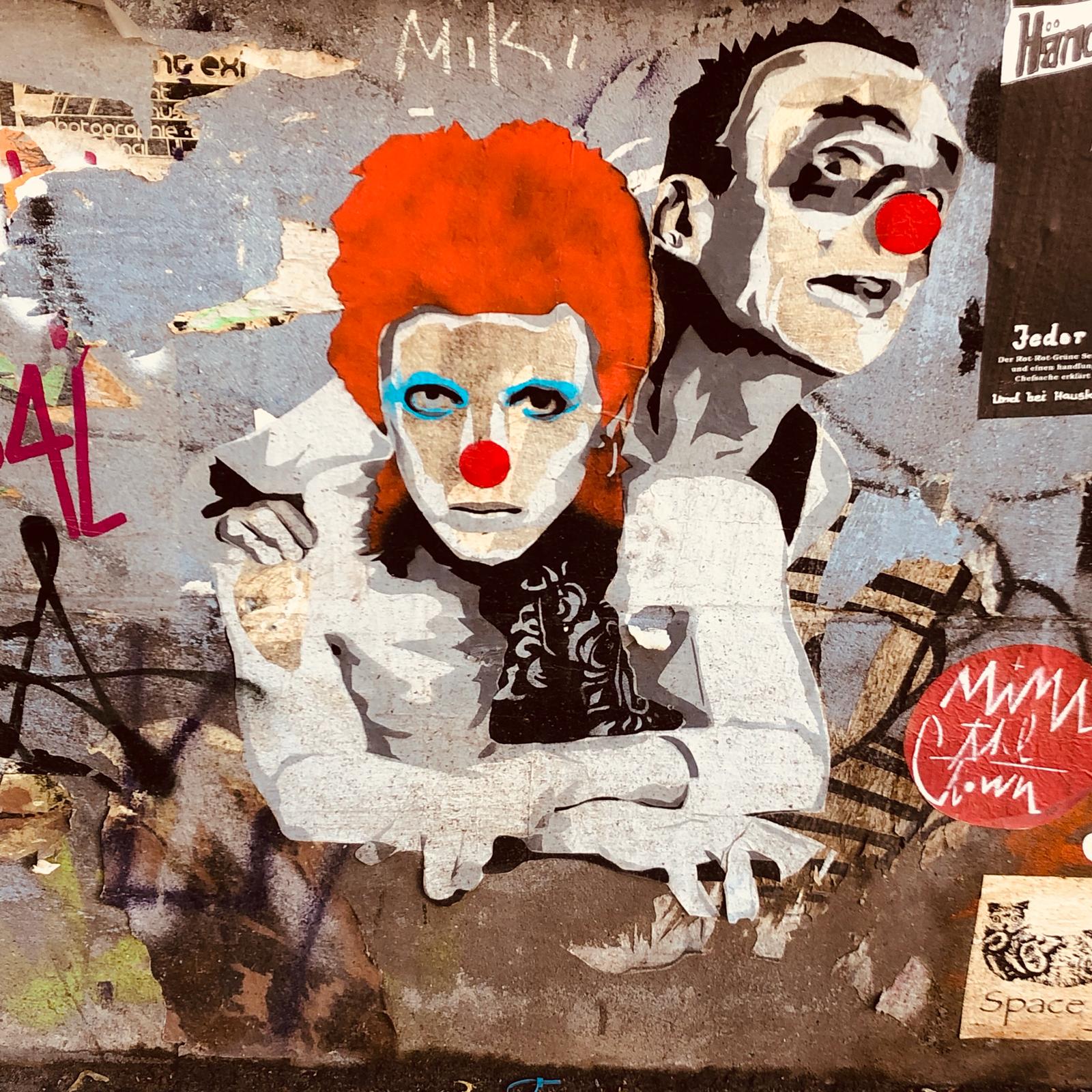 Street-art image of David Bowie as Ziggy Stardust and Mimi the Clown painted on a weathered Berlin wall.